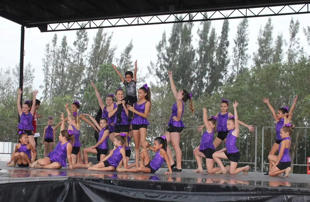 Studio 8 dancers in purple sequin costumes performing on an outdoor covered stage