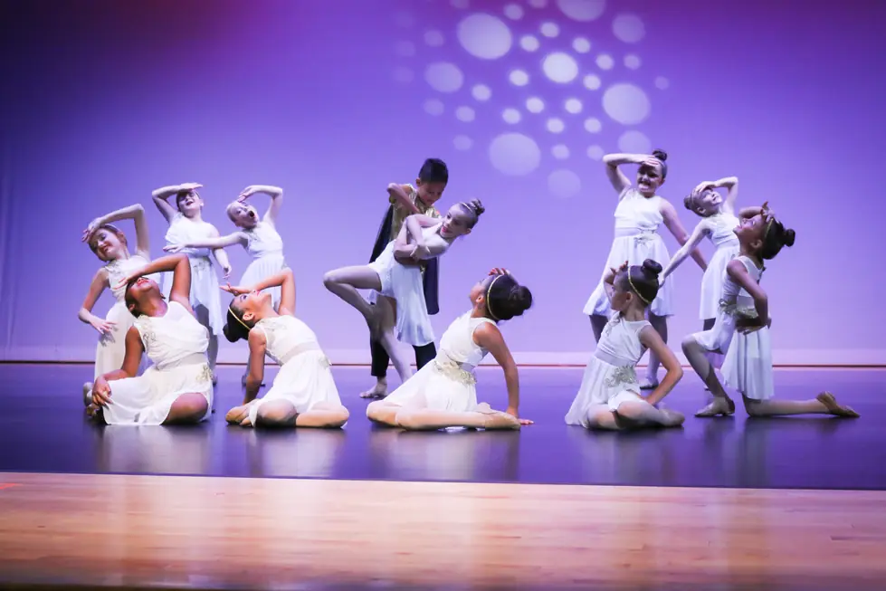 The full Studio 8 company in white and gold costumes posed across the stage under a purple wash